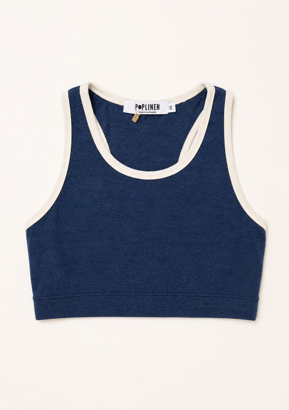 A navy blue cropped tank top with cream-colored contrast trim, laid flat against a light cream background. The brand label 'Poplinen' is visible inside the collar.