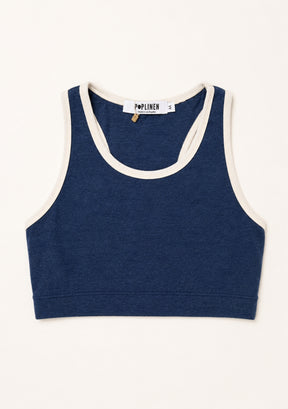 A navy blue cropped tank top with cream-colored contrast trim, laid flat against a light cream background. The brand label 'Poplinen' is visible inside the collar.