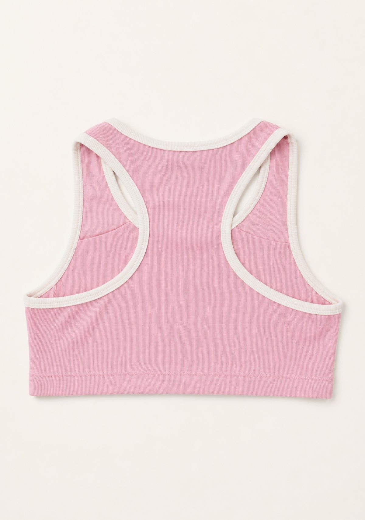 A pink cropped tank top shown from the back, featuring contrasting white trim along the racerback straps and neckline, laid flat against a light cream background.